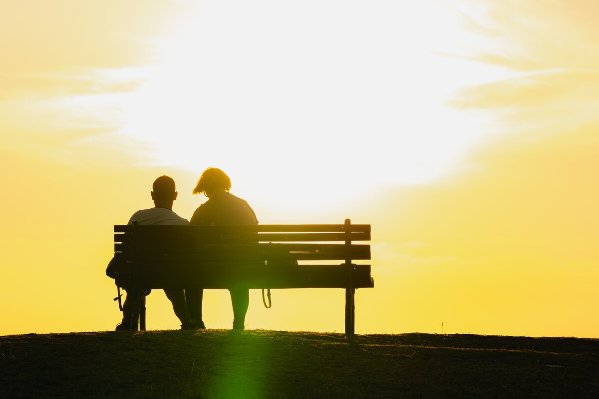Two people silhouetted on a bench against a blazing golden sunset