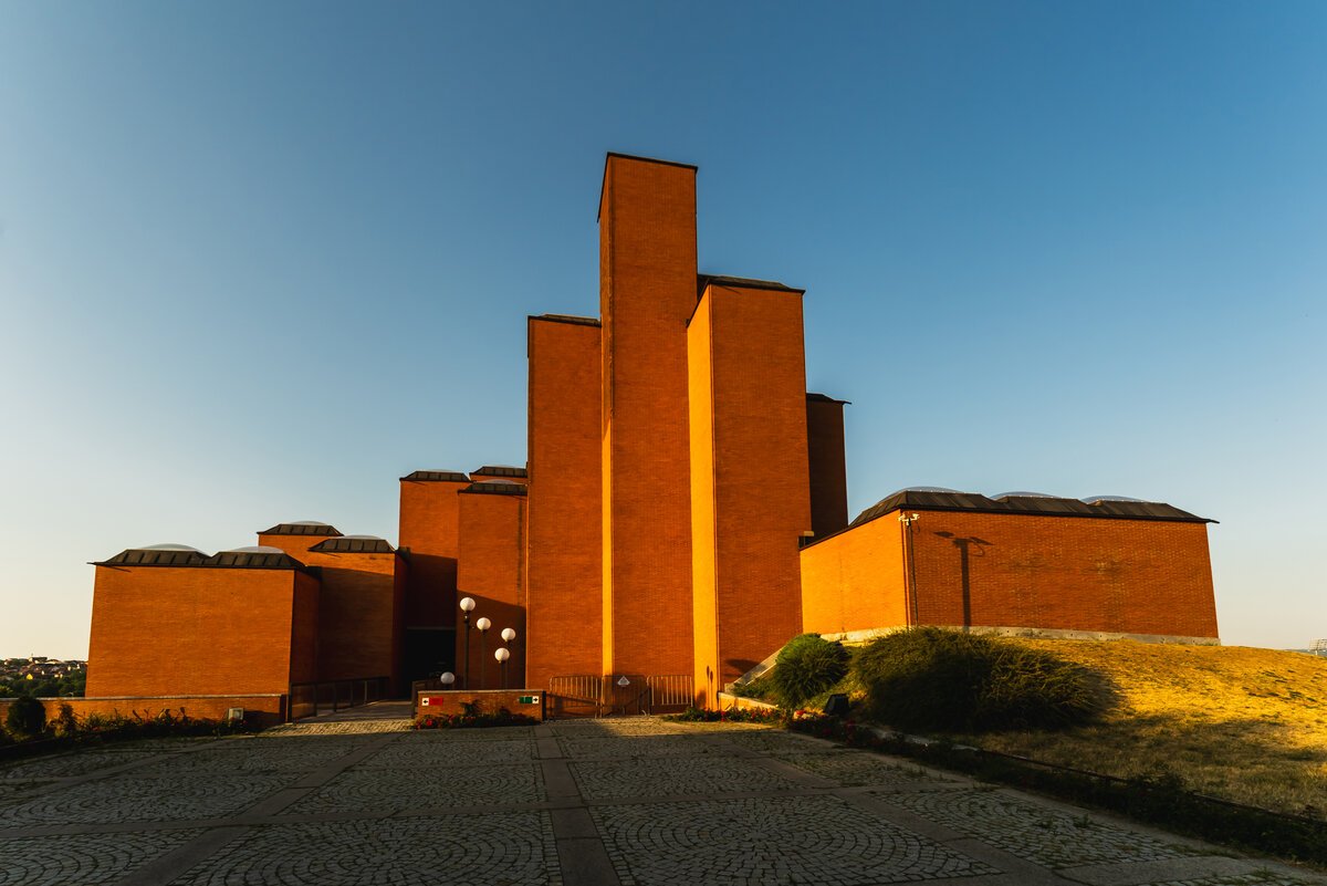 Brutalist red-brick building (Museum of Aviation / monument-style structure) against deep blue sky at golden light