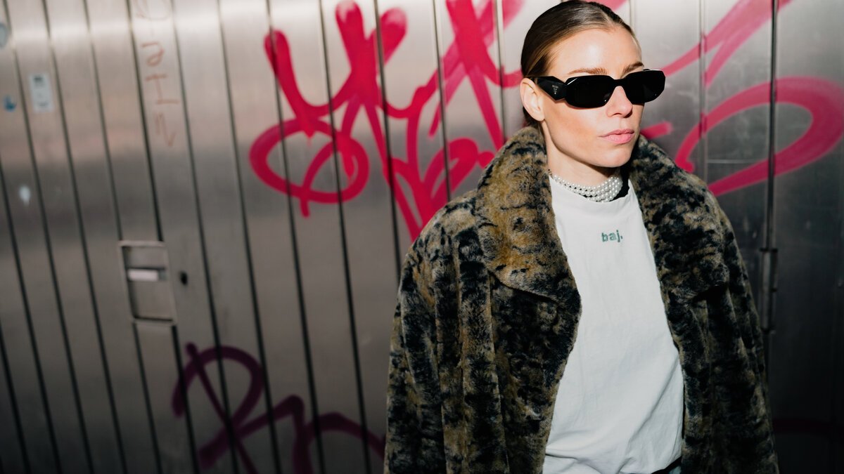Woman in animal-print fur coat & sunglasses against graffiti metal shutter