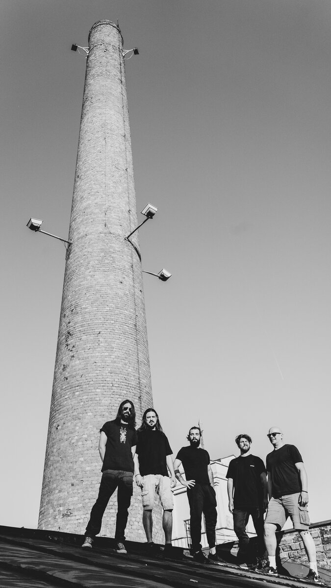 Group of five men (band/crew) at base of tall brick chimney, low angle