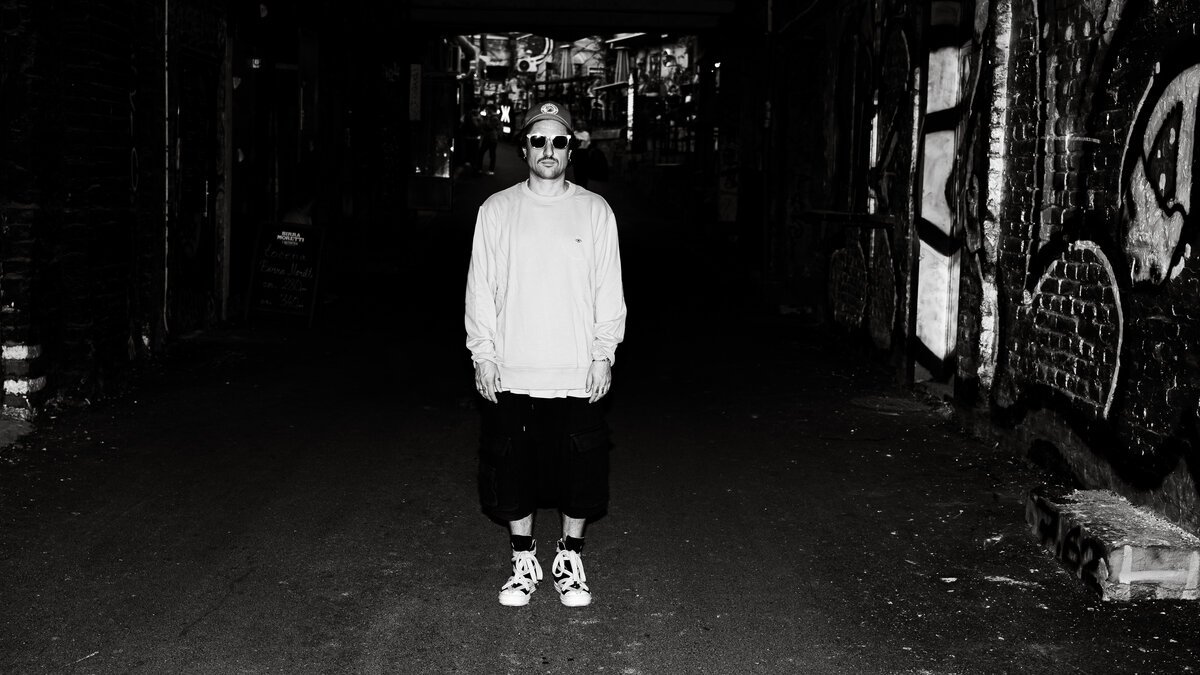Man in white sweatshirt standing in dark graffiti alley
