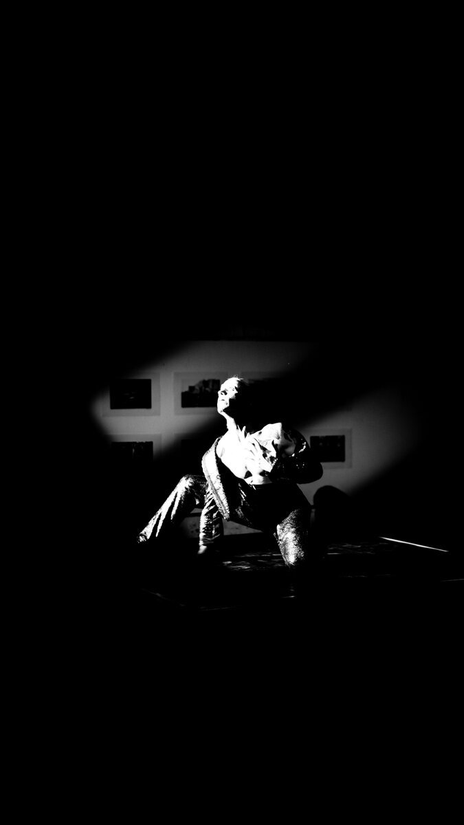 Crouching figure spotlit in a dark stage/space, dramatic movement