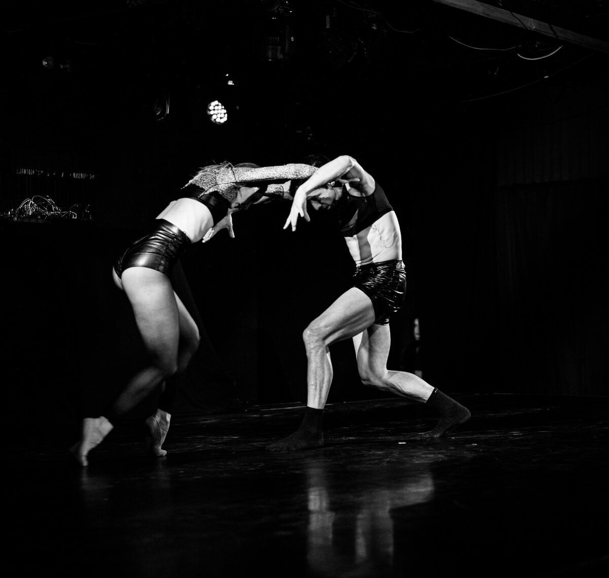 two dancers mid-movement on a dark stage, contorted pose