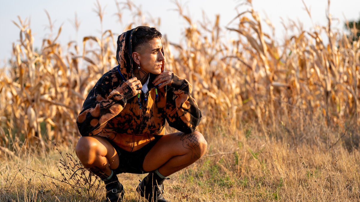man crouched in dried cornfield wearing bleach-dyed tie-dye hoodie