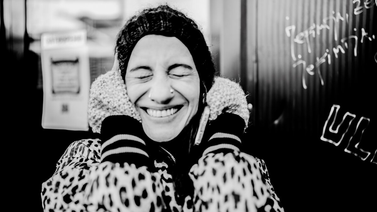woman laughing with eyes closed, hood up, leopard-print coat, B&W street