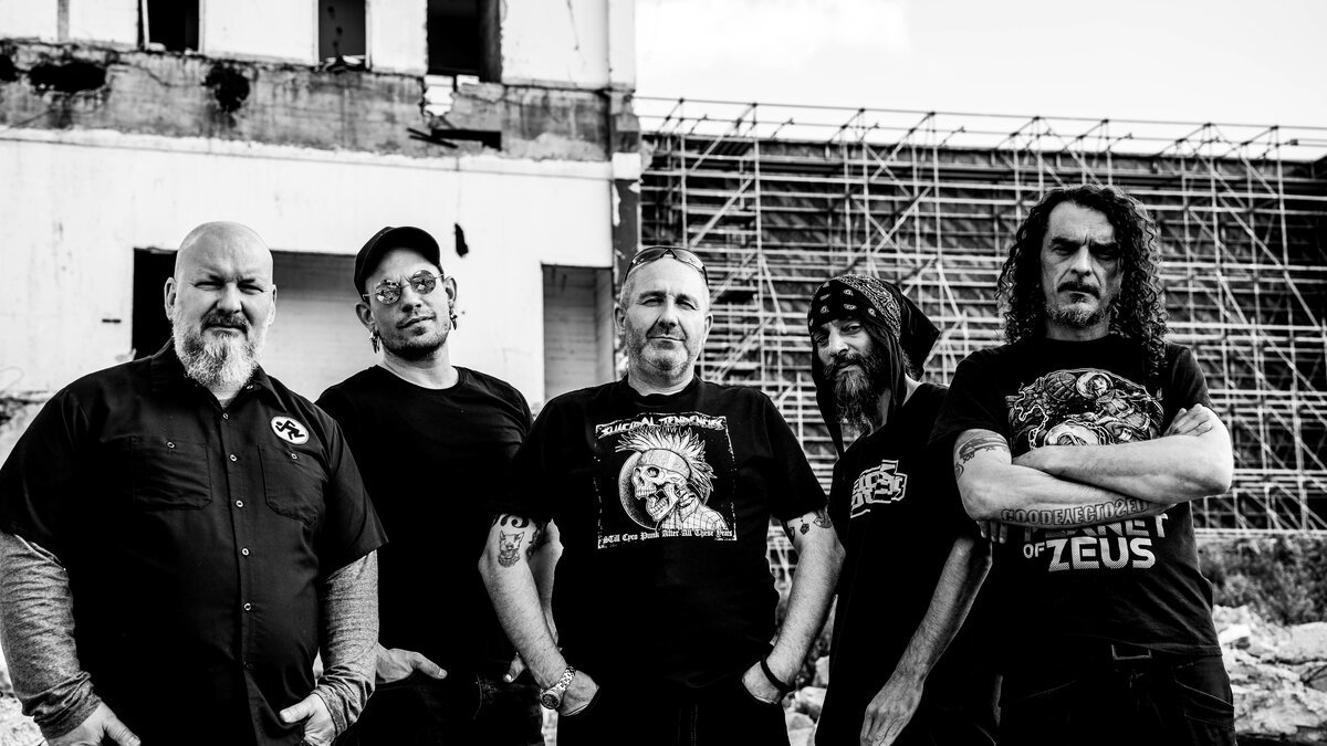 same five-member band group portrait, B&W, ruined-building backdrop