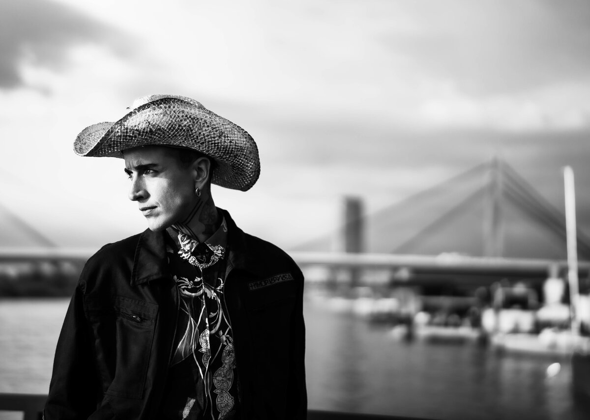 young man in straw cowboy hat and scarf, B&W, cable-bridge riverside backdrop