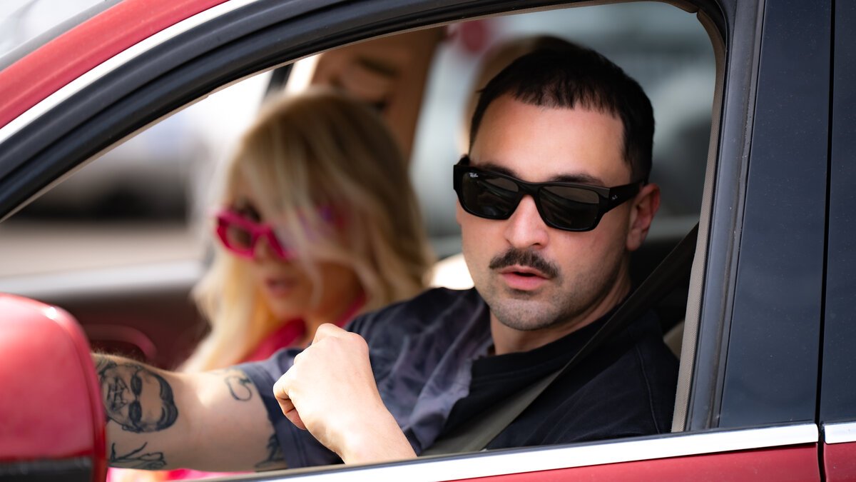Two men and a woman in a red car, sunglasses, tattoos