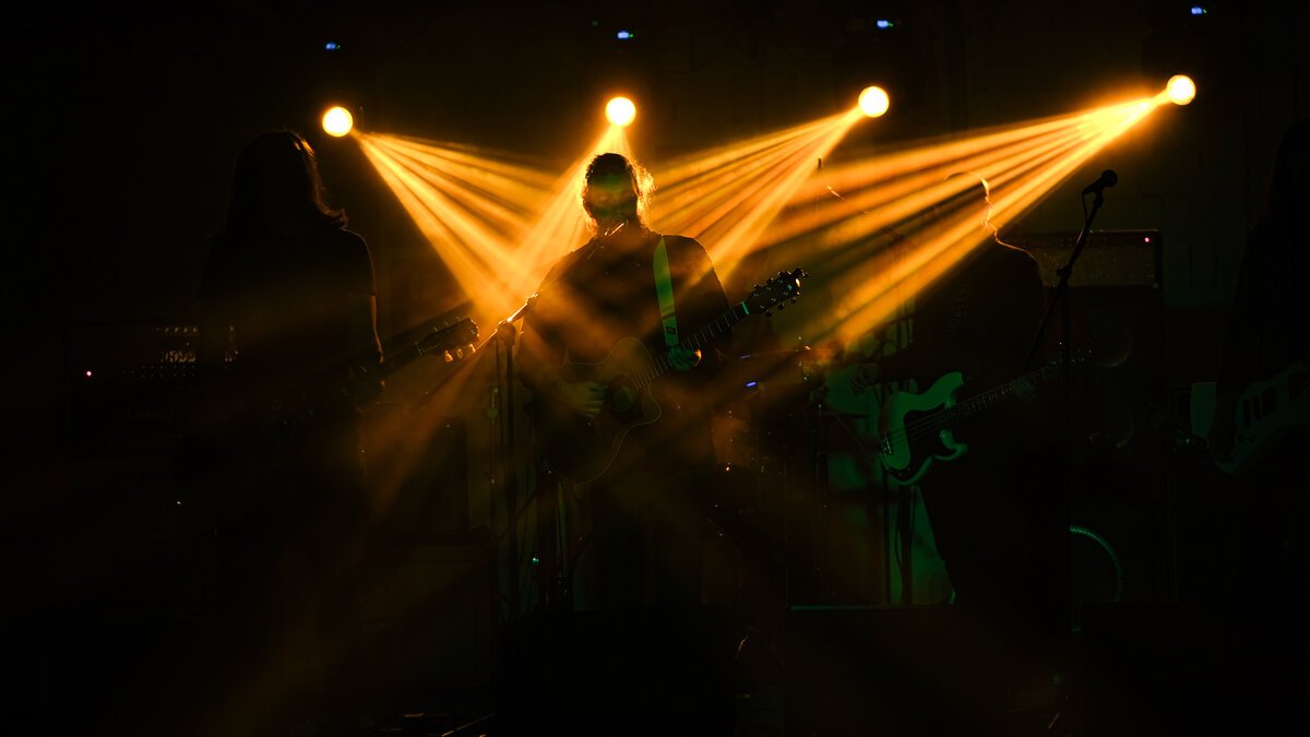 Band on stage silhouetted, bassist center, golden fan-beam stage lights