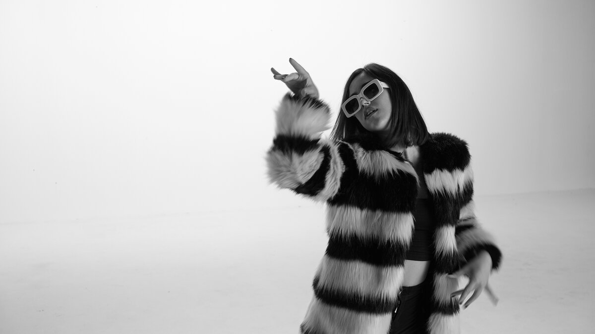 Woman in striped fur coat and white sunglasses posing on white seamless