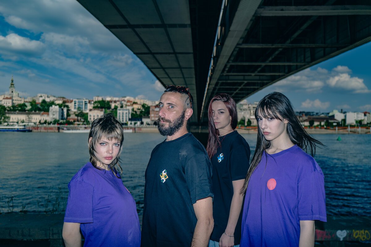group of four in purple/black Crooked tees under bridge, Belgrade skyline behind