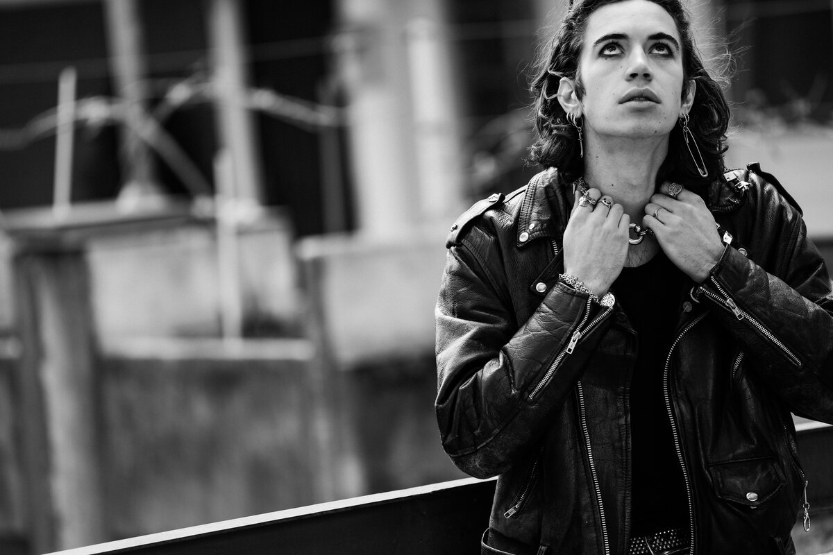 young man in leather jacket and rings, gazing upward, industrial backdrop