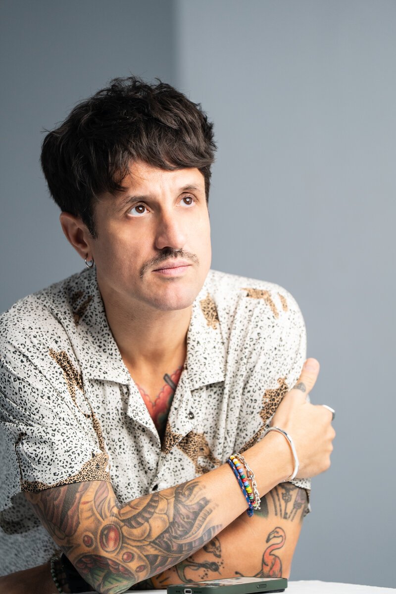 tattooed man with mustache in printed shirt, looking up, at a table