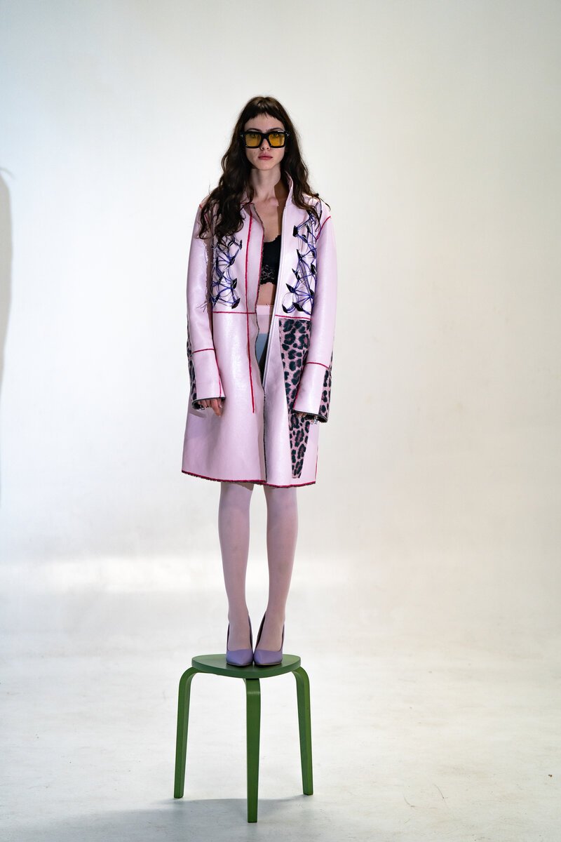 model in pale-pink printed coat and sunglasses standing on a green stool, white seamless