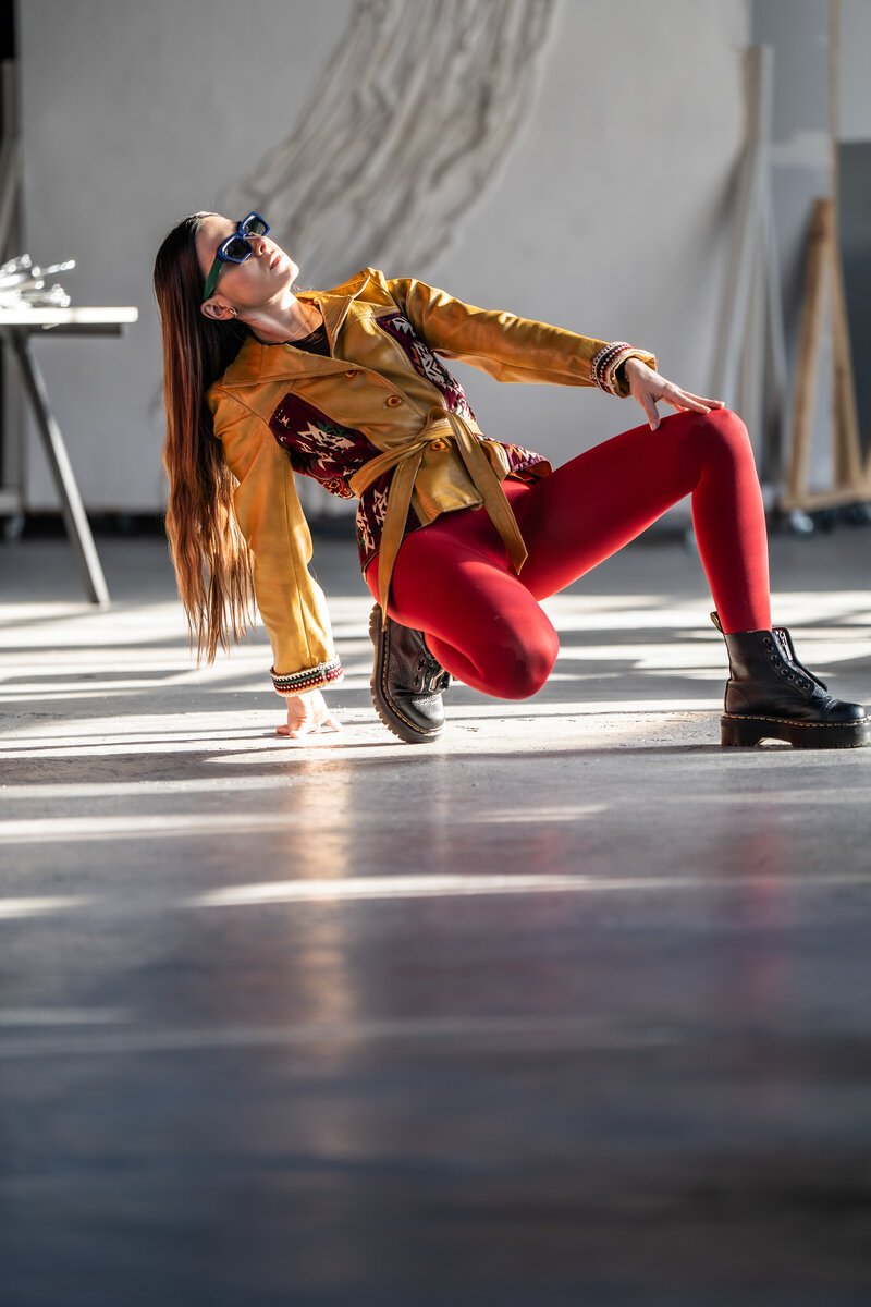 woman in yellow suede jacket, red tights and boots reclining/dancing in sunlit loft